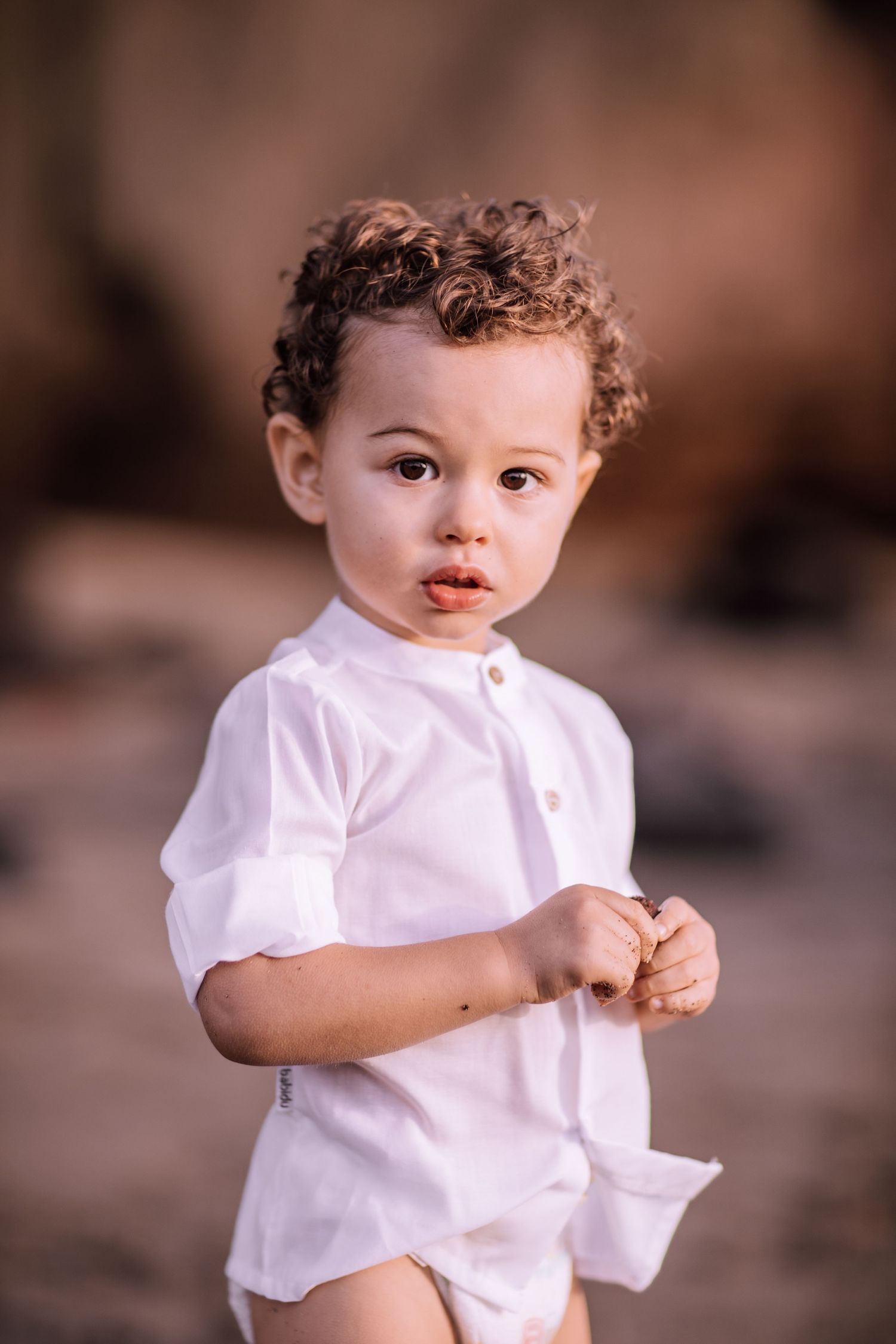 Toddler in white shirt plays outdoors on warm sunny day.