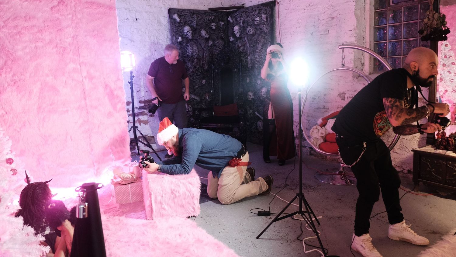 Photography crew working with lighting equipment in a pink-walled studio space.