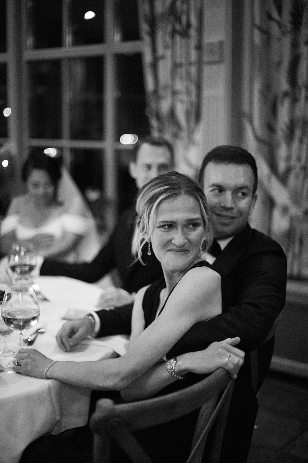 A black and white candid photo shows wedding guests seated at tables during a reception celebration.