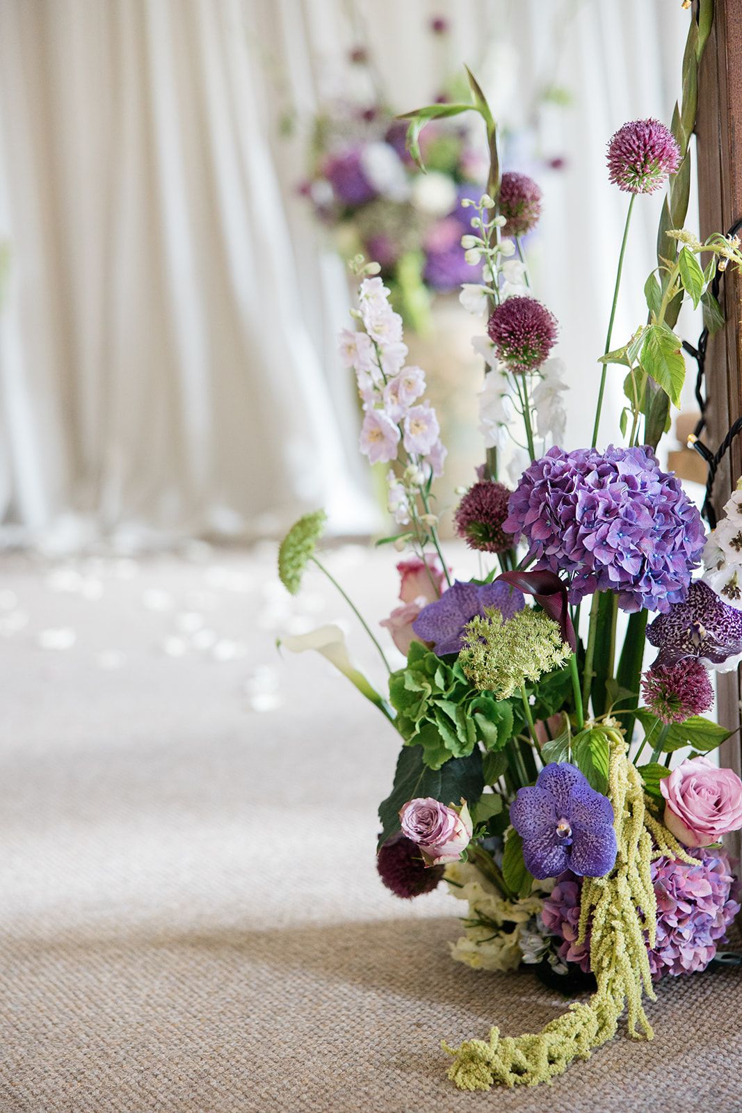 Close-up view of purple hydrangeas and pink roses arranged with delicate greenery on a rustic burlap tablecloth.