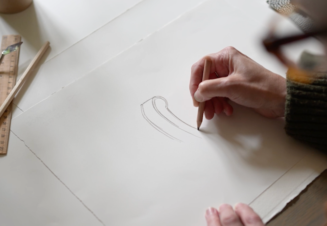 Close-up view of hands sketching on white paper with a pencil.