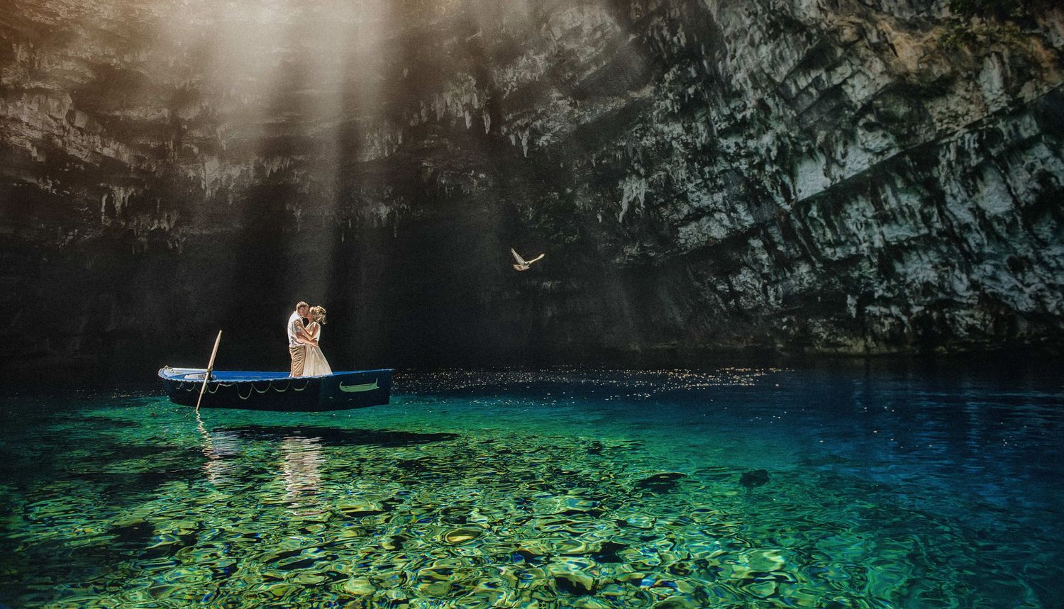 Wedding couple in boat glides through stunning crystal clear turquoise cave waters.