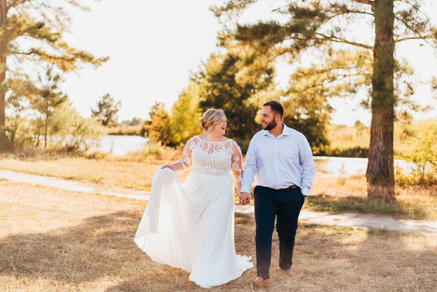 Couple walking hand in hand through a sunlit forest path during golden hour.