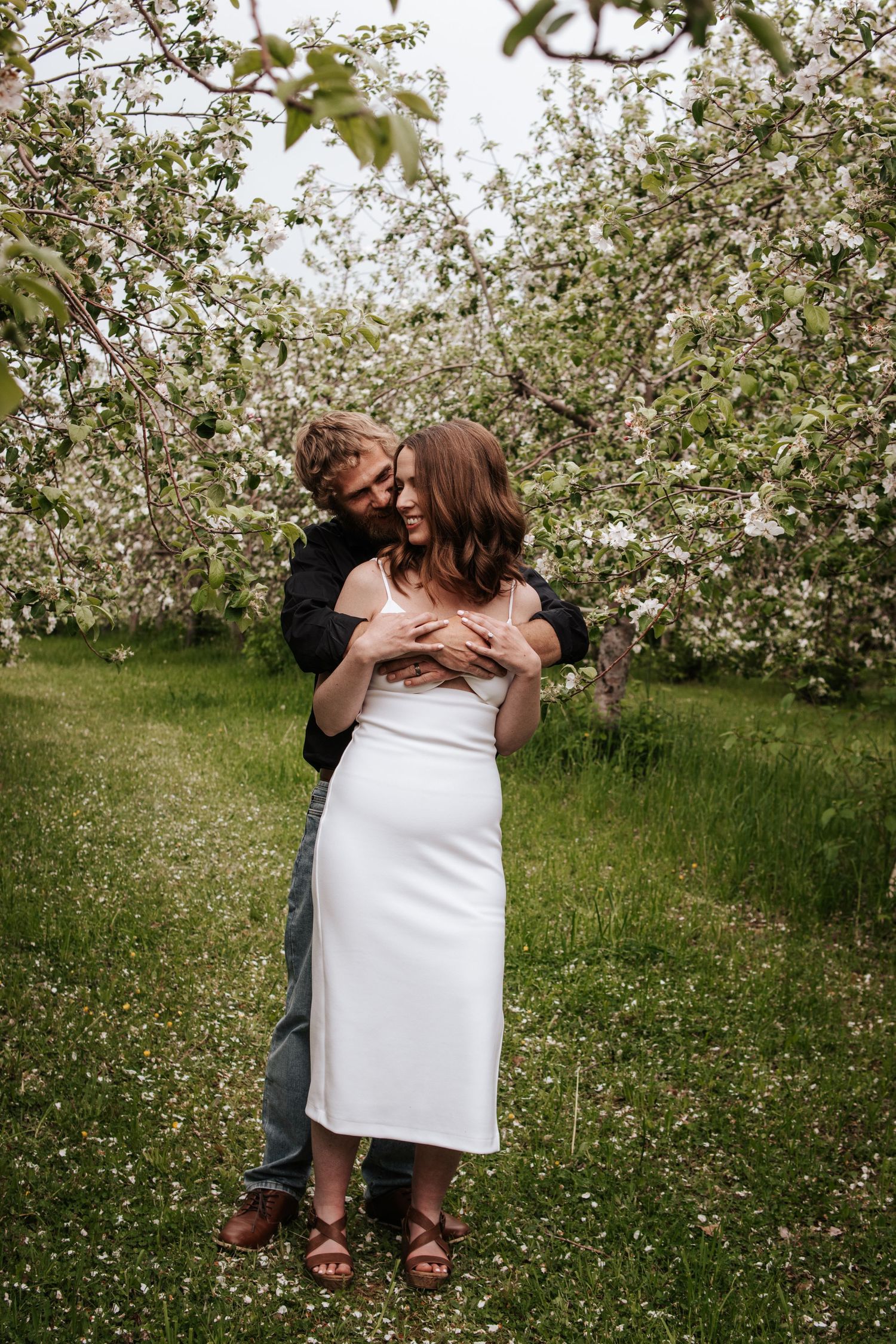 A romantic moment shared between a couple embracing in a blooming spring orchard with white flowers.