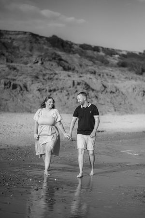 A couple walks together along a beach shoreline in black and white photography.