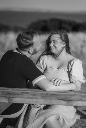 A romantic black and white photo series of a couple sharing intimate kisses while leaning against a wooden fence.