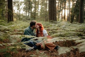 Romantic couple lounging together on mossy rocks in a sunlit forest during golden hour.