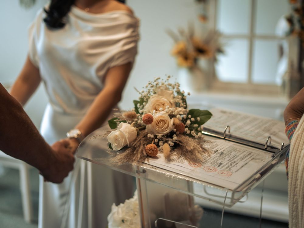 A delicate peach and blush rose wedding bouquet rests on a clear acrylic podium during an indoor ceremony in Naples, Florida