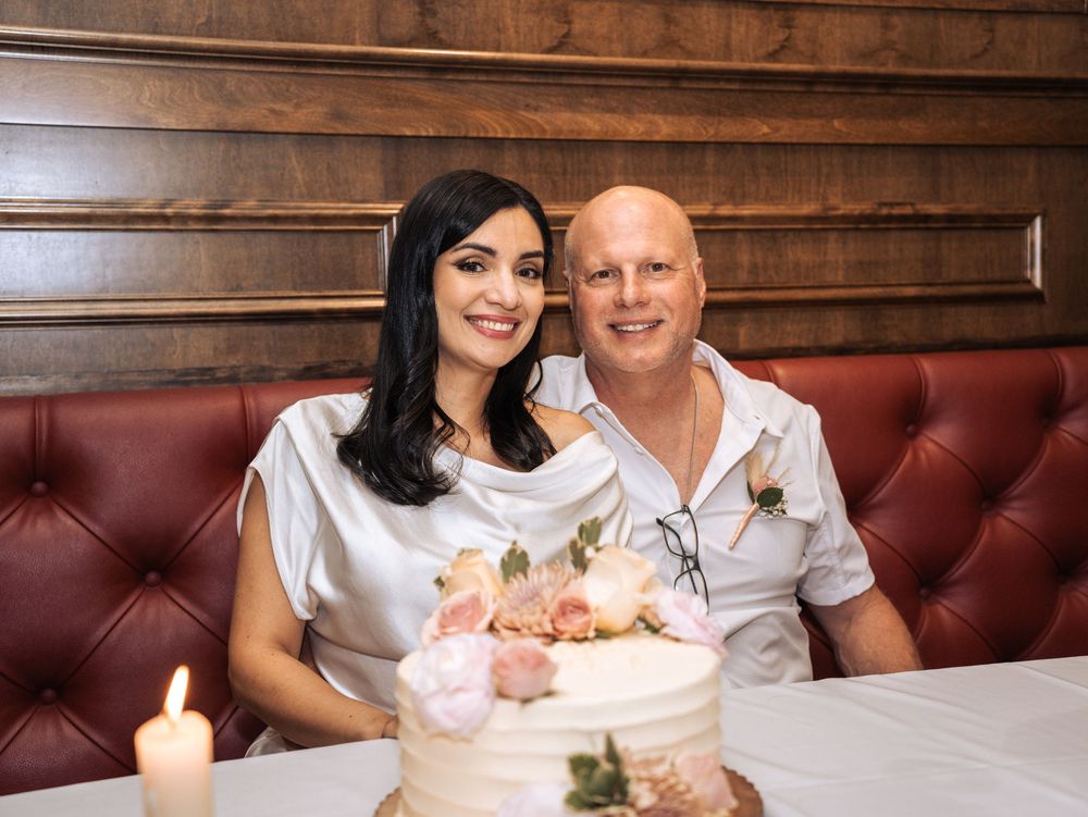 A couple sits together on a red leather booth smiling while celebrating with a decorated cake in Naples, Florida
