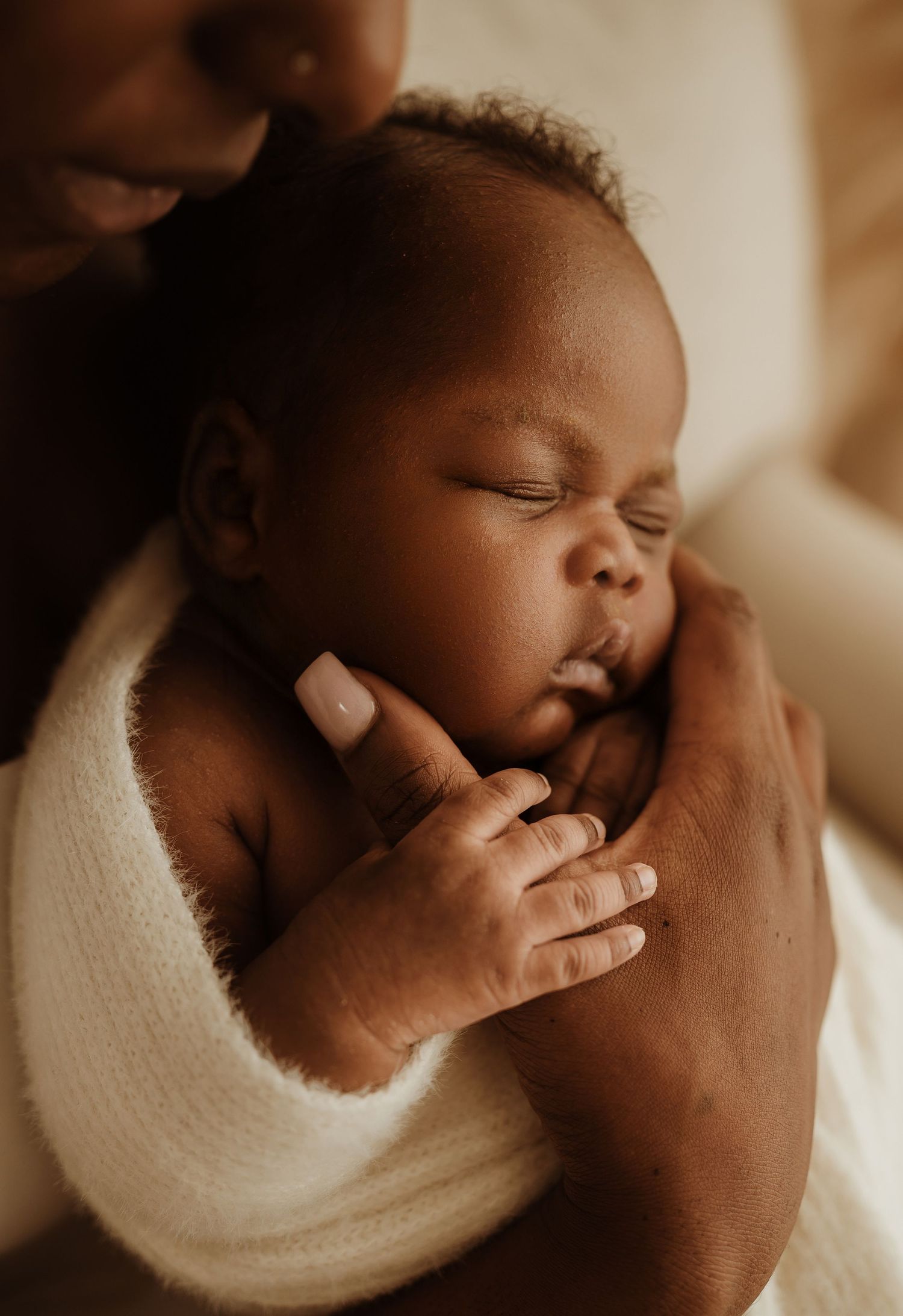 A sleeping baby wrapped in white fabric is tenderly cradled in gentle hands.