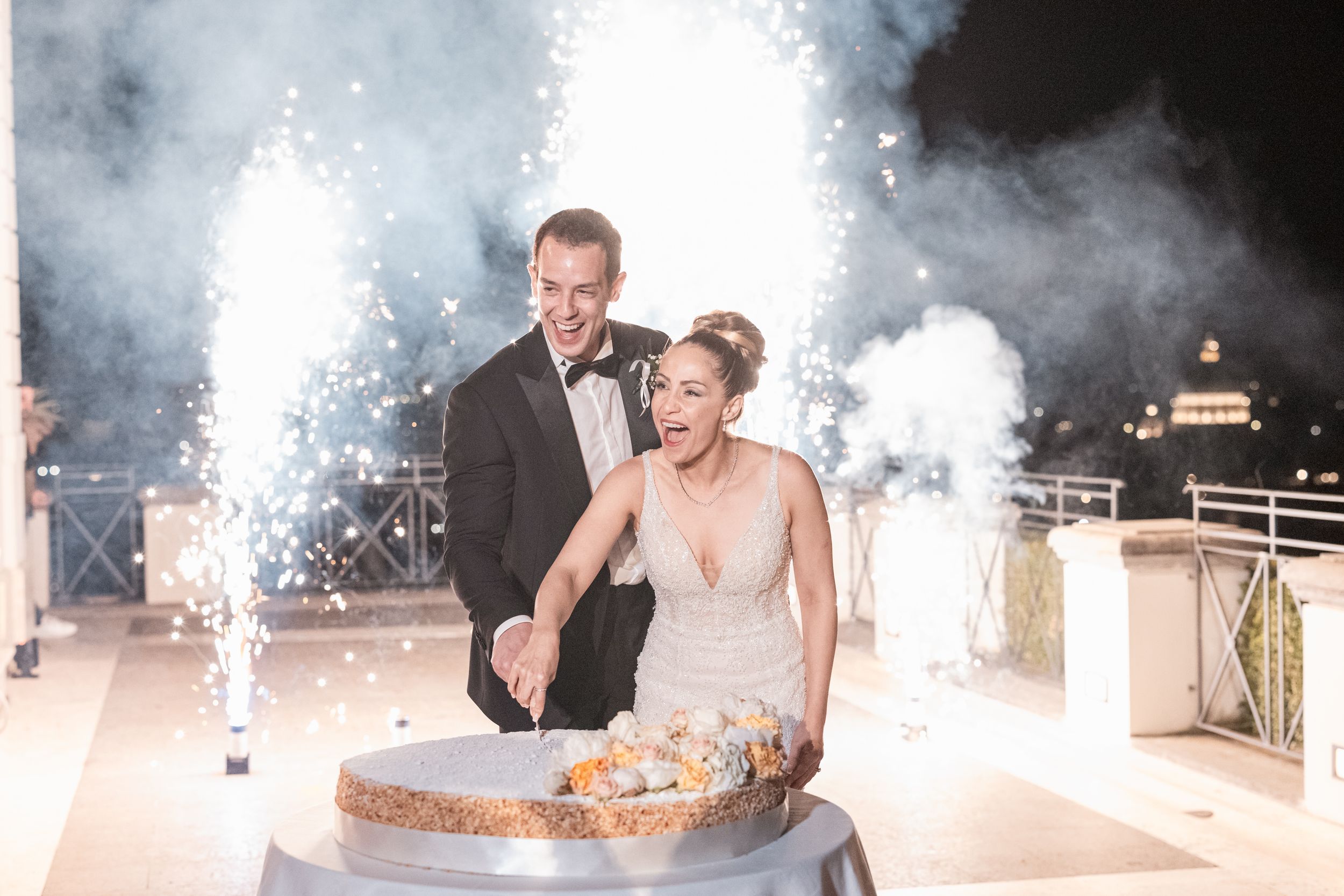 Newlyweds share their first dance surrounded by sparklers and smoke effects at an evening wedding reception.