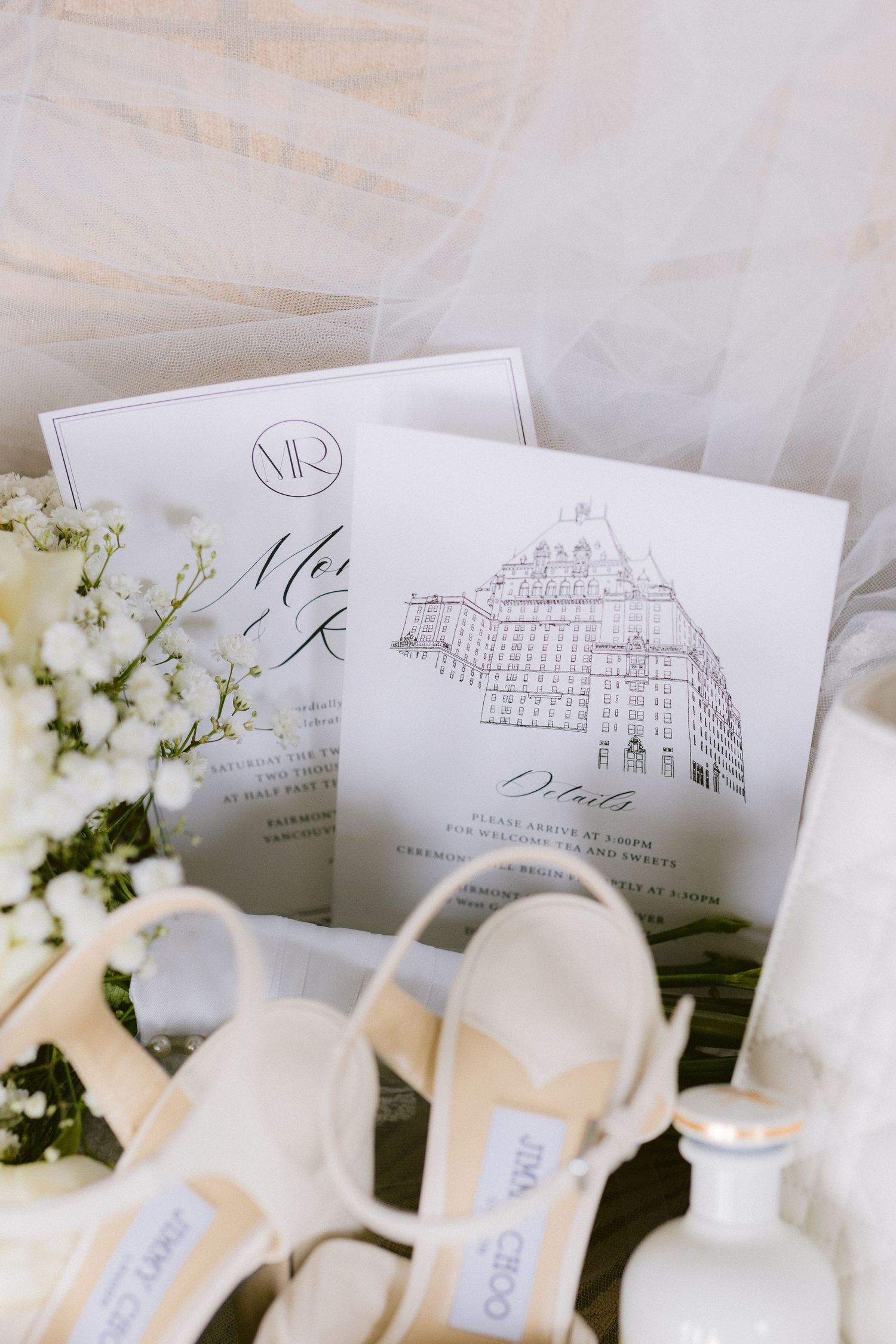 Elegant wedding invitations with Fairmont Hotel Vancouver displayed alongside white floral arrangements and place cards.