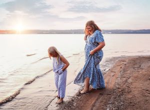 People playing and walking along a sandy beach at sunset with calm waters in the background.