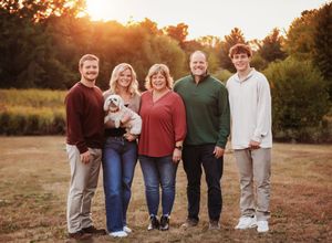 Family members stand together on a grassy hill at sunset wearing coordinated casual outfits.