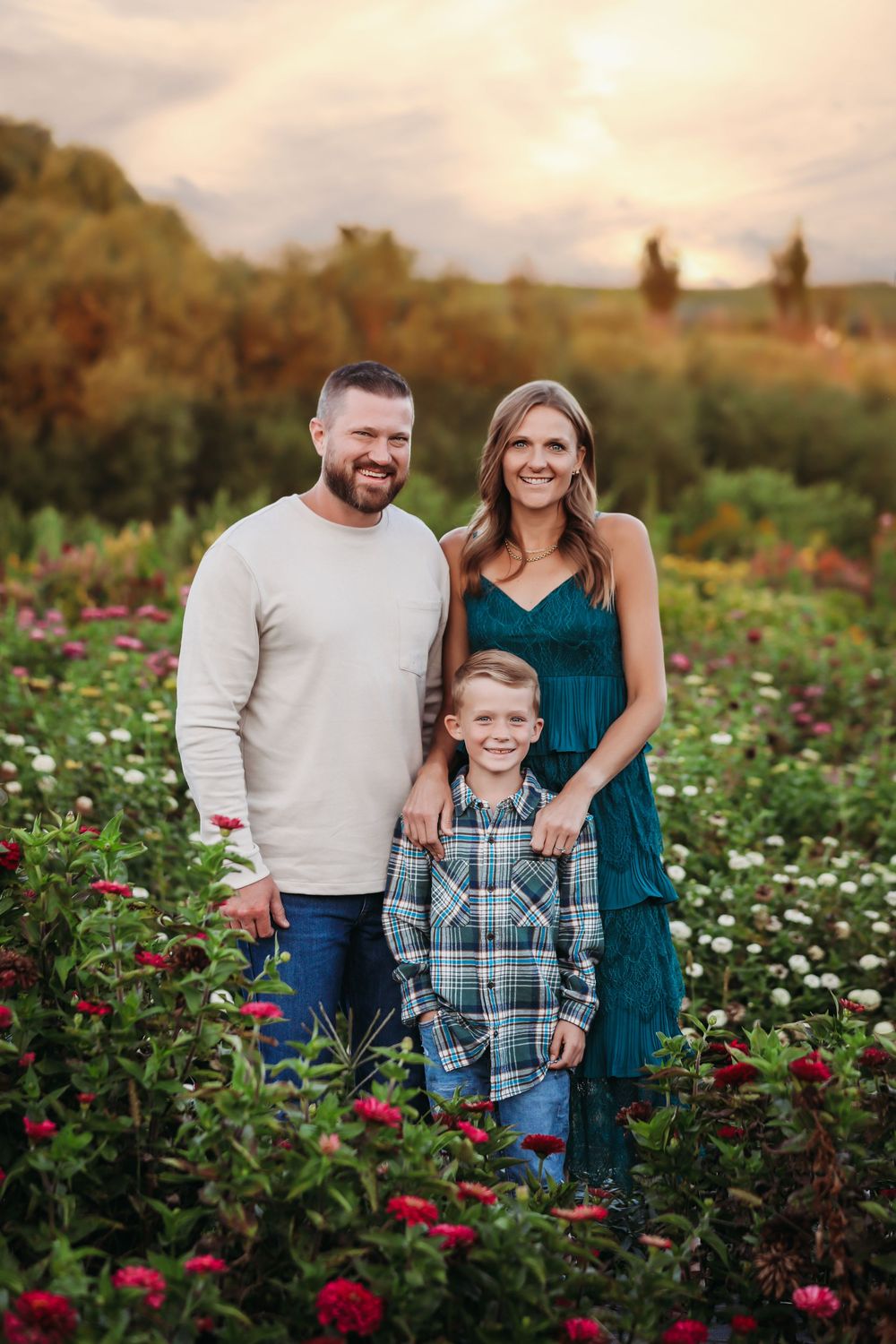 Family of three standing together in a blooming flower garden at sunset.