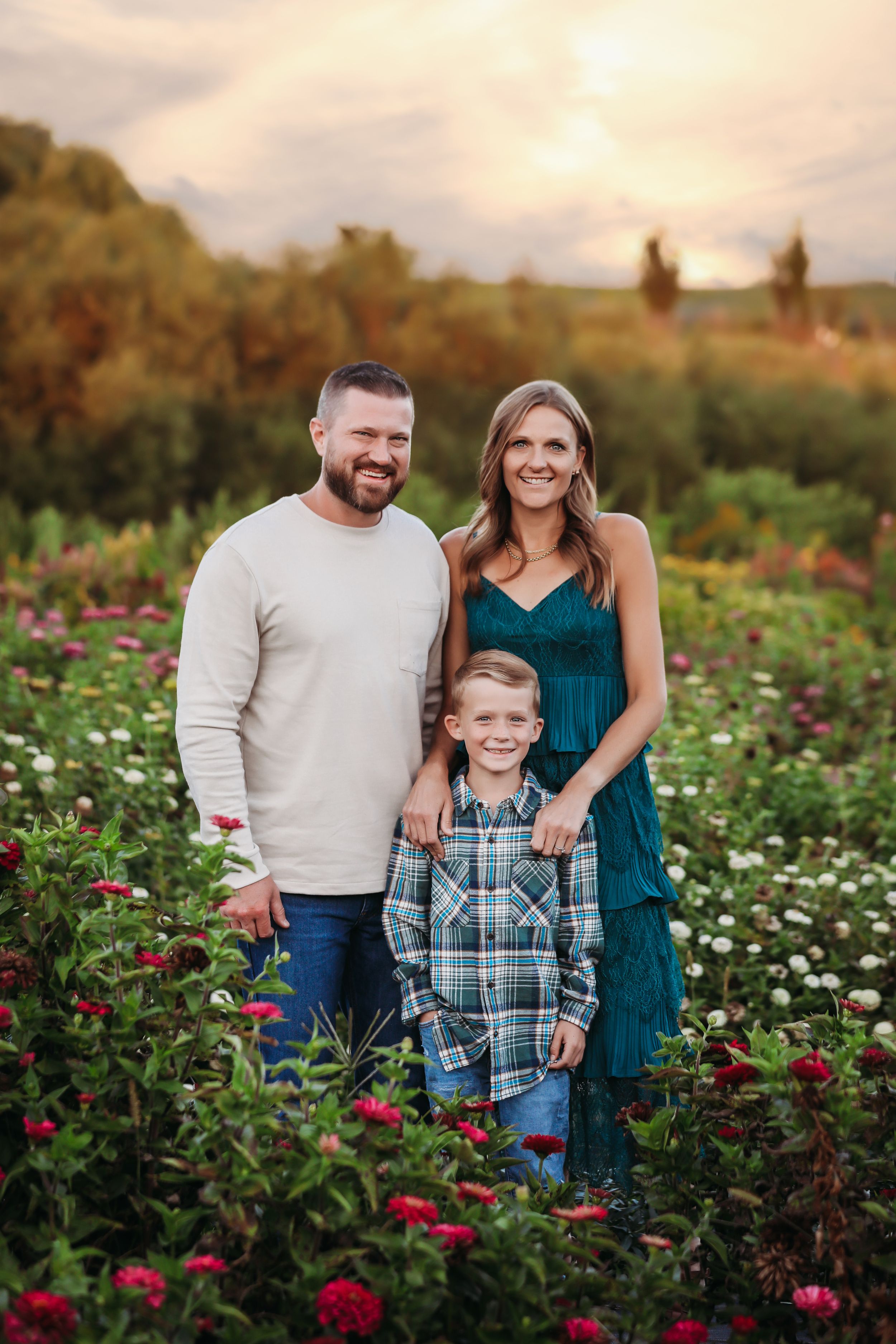 Family of three standing together in a blooming flower garden at sunset.