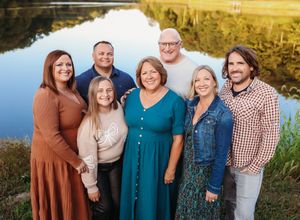 Group portrait by a lake with people wearing coordinated fall colors and casual attire.
