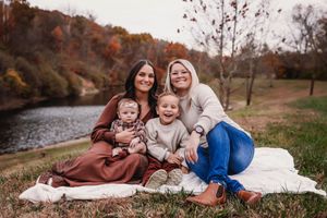 Family sitting on blanket by riverside during autumn season.