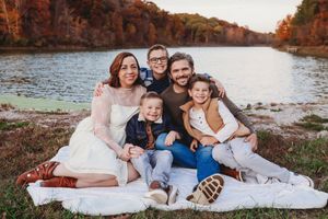 Family sitting together on white blanket by autumn lake during sunset photoshoot.
