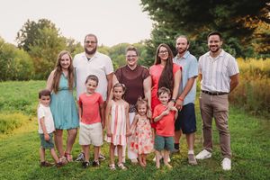 Large family group portrait taken outdoors in a grassy field during golden hour.