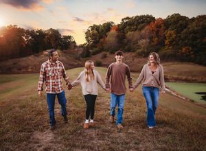 Multiple people walk hand-in-hand across a grassy hill during sunset.