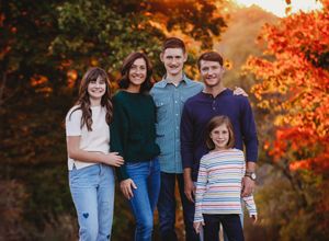 Family gathering outdoors during autumn with vibrant fall foliage in the background.