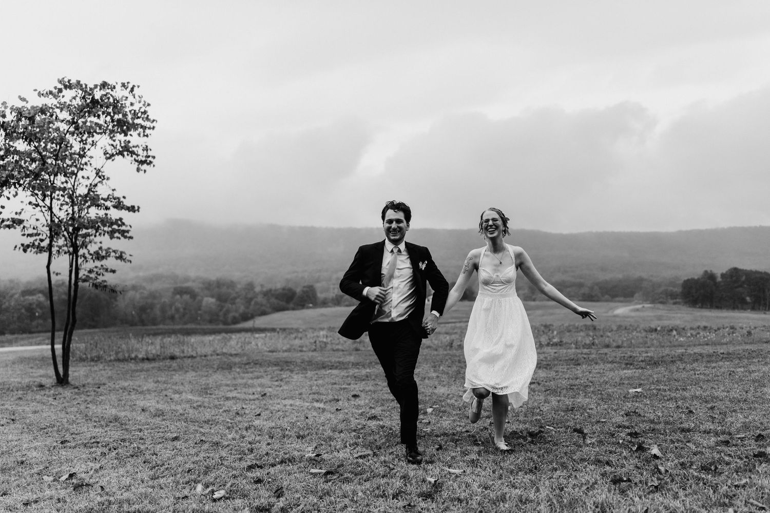 A bride and groom runs joyfully through a hilltop meadow from elopement photoshoot in Harrisburg, PA.