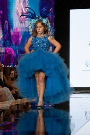A model walks the runway in a bright blue tulle dress with sequins at a fashion show.