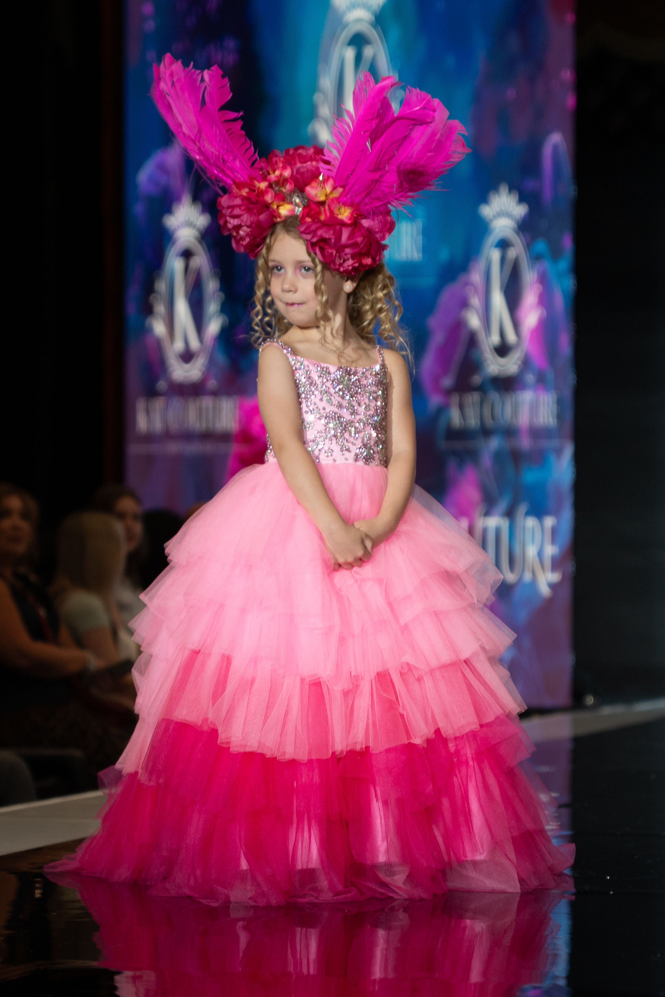 A model walks the runway in a dramatic pink ombre tulle gown with hot pink feather headpiece at a fashion show.