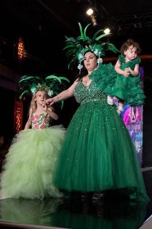 Models wearing sparkly green formal dresses and tutus perform on stage during a fashion show.