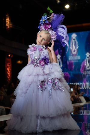 Elegant white and purple tulle ball gown with floral accents showcased at a fashion event under dramatic lighting.