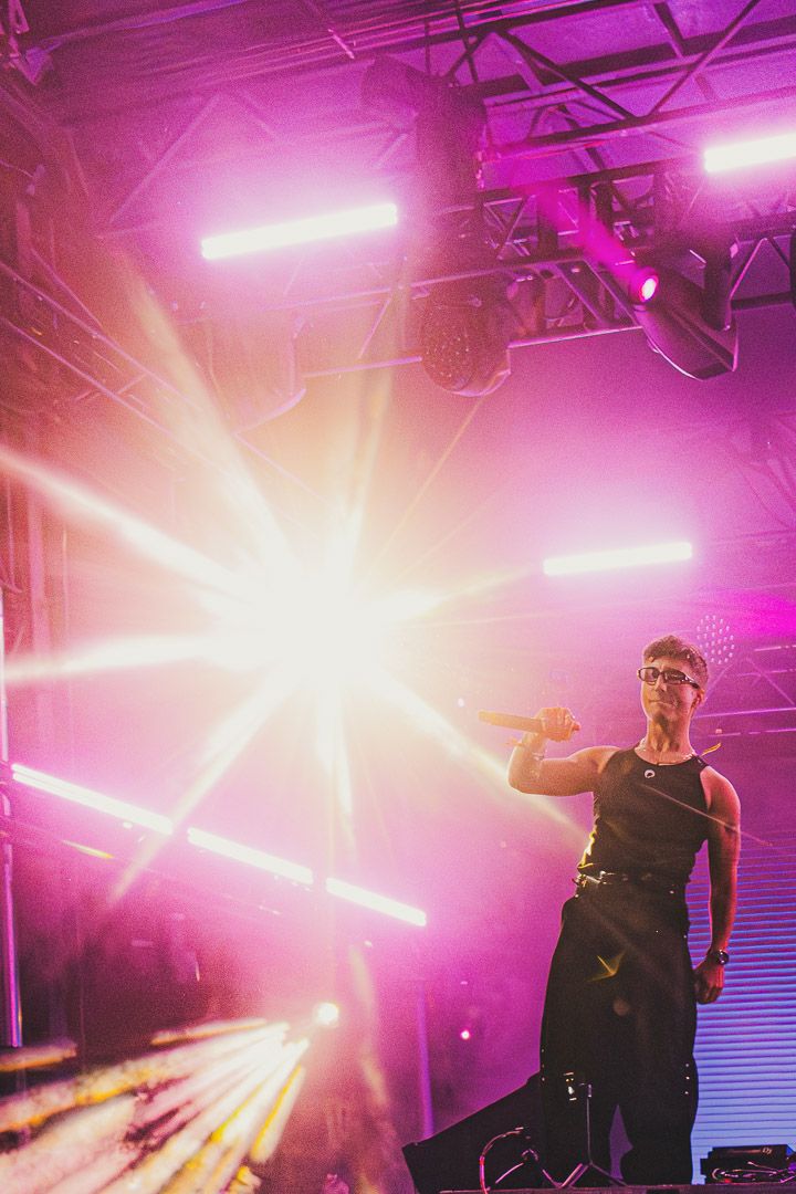 Concert stage illuminated with dramatic pink and purple lighting creating an atmospheric performance environment.