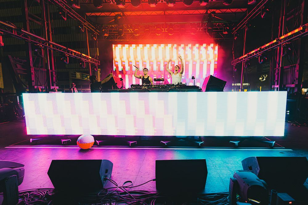 Concert stage with red lighting and illuminated vertical panels creating a striking visual display.