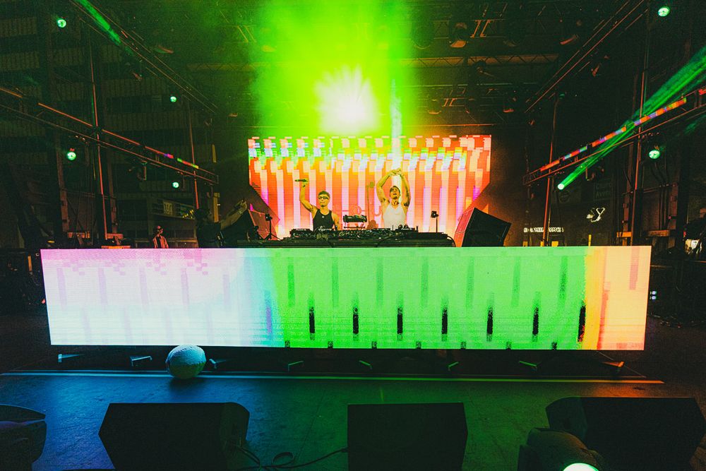 Stage design featuring bright green lighting and multicolored LED panel backdrop.