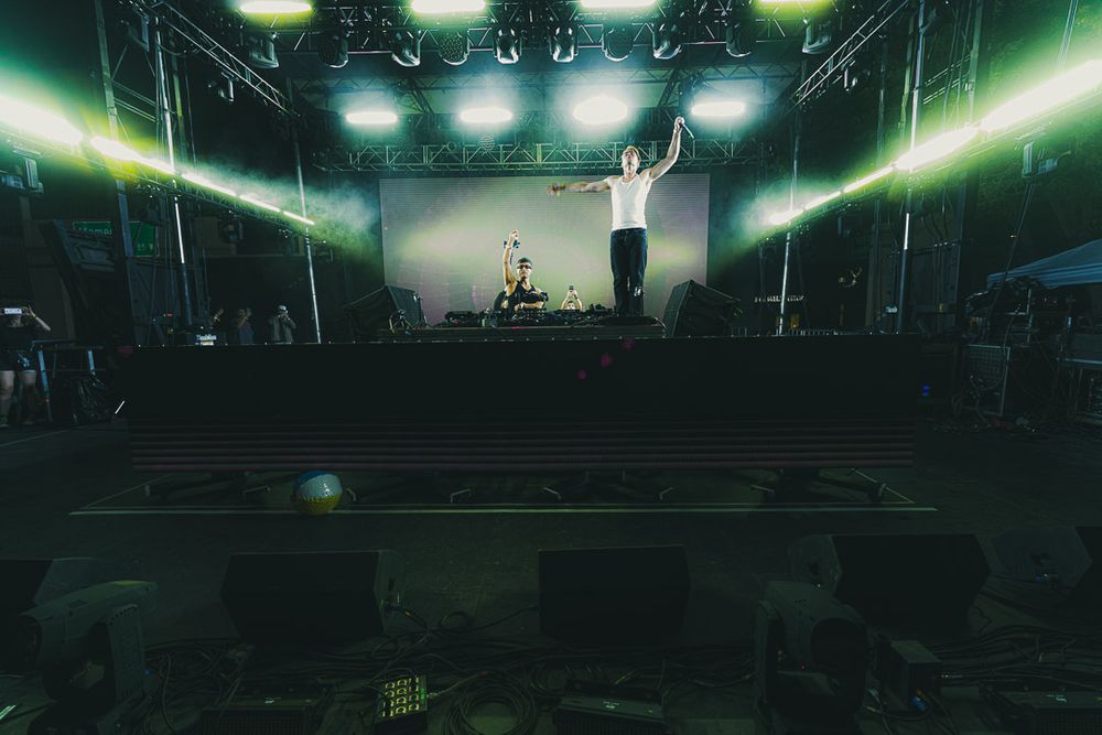 A dark green atmospheric concert venue with dramatic stage lighting and silhouetted figures performing on stage.