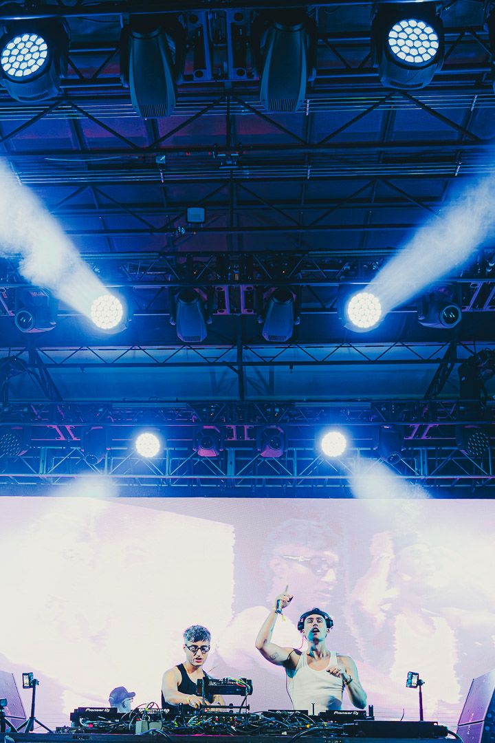DJs perform on stage with dramatic blue lighting and smoke effects at an electronic music concert.