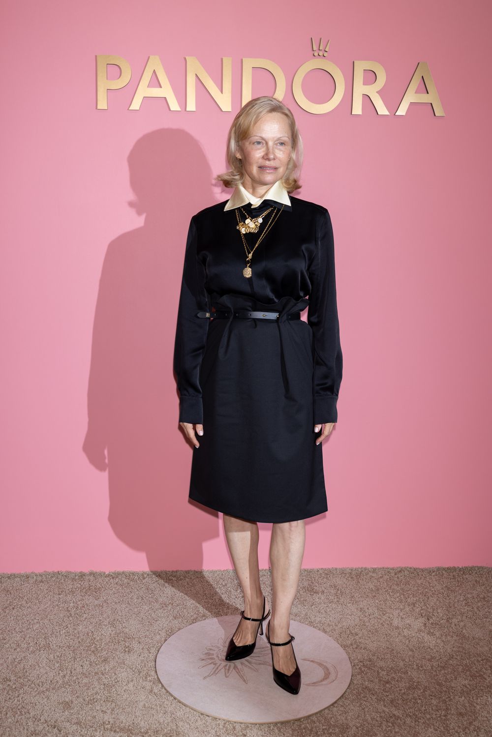 A person in a black outfit stands against a pink backdrop at what appears to be the Pandora event.