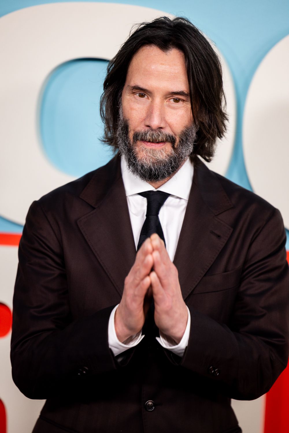 A series of four photos showing someone in a black suit making prayer-like hand gestures against a light blue background.