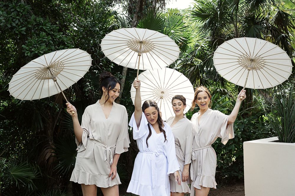 Bridesmaids holding white parasols in tropical garden at Grand Palladium Riviera Maya.