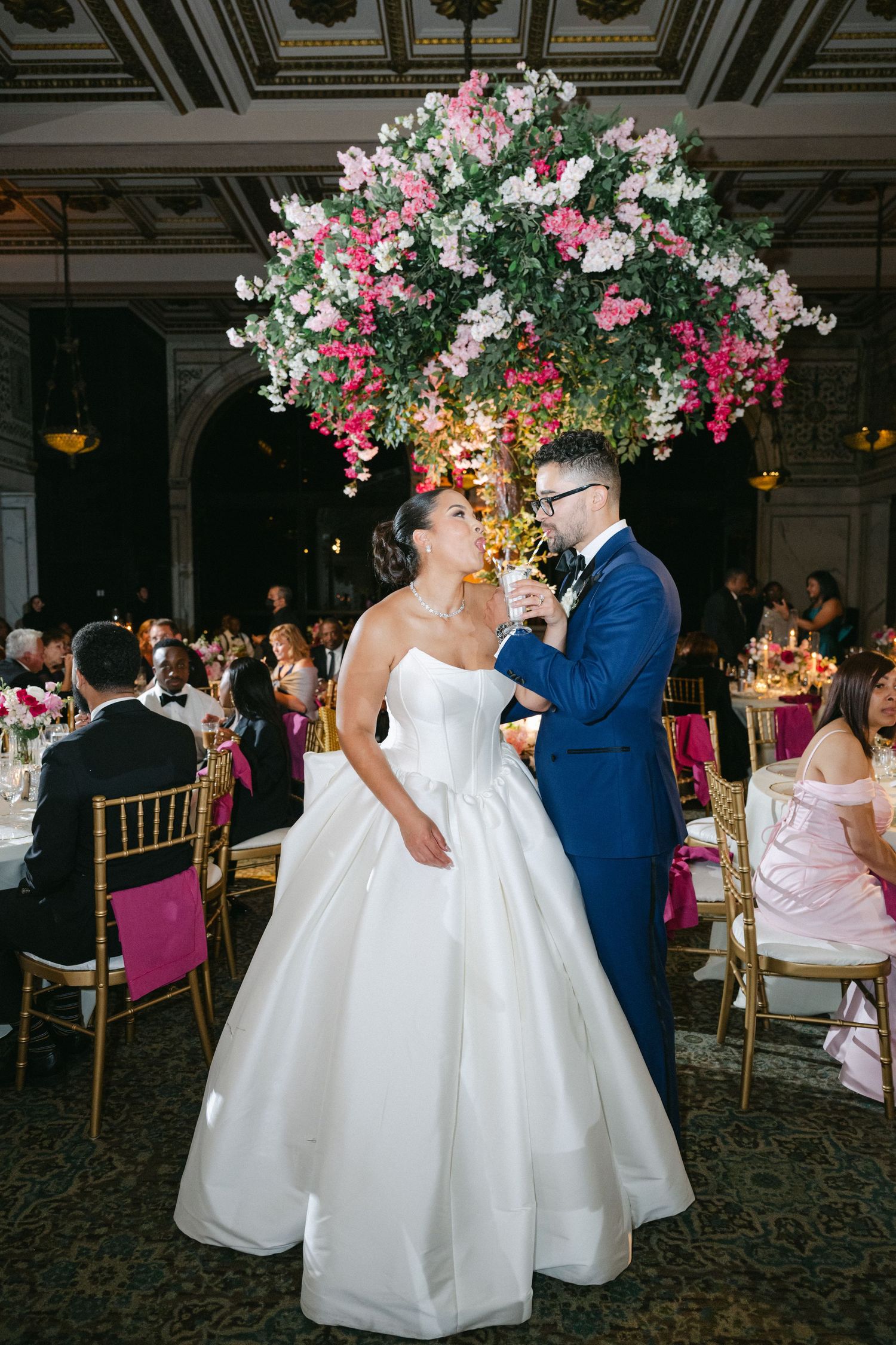 Wedding couple dancing together under pink and white floral decorations in an elegant ballroom reception venue.