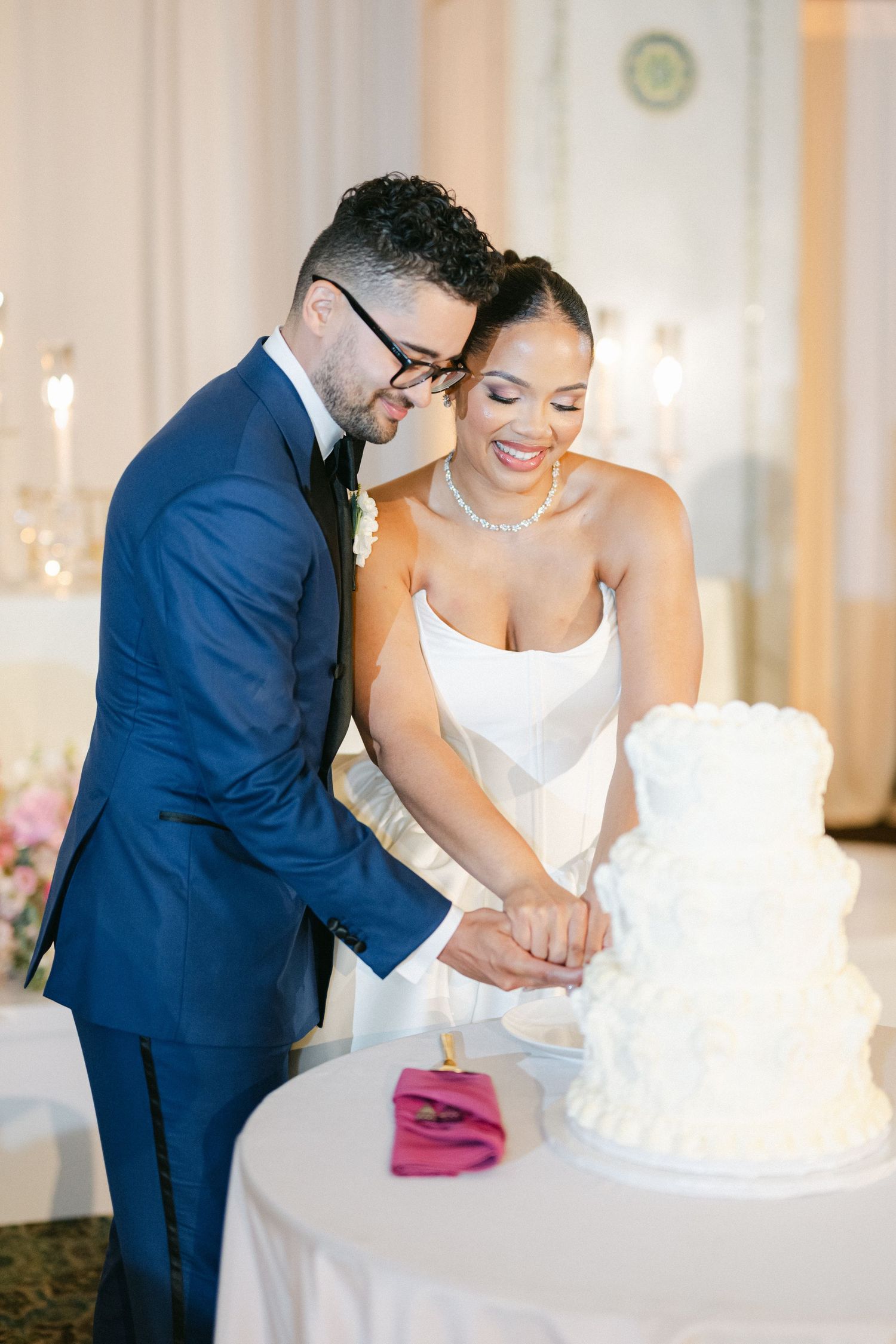 A couple in wedding attire cut their white wedding cake together during their reception celebration.