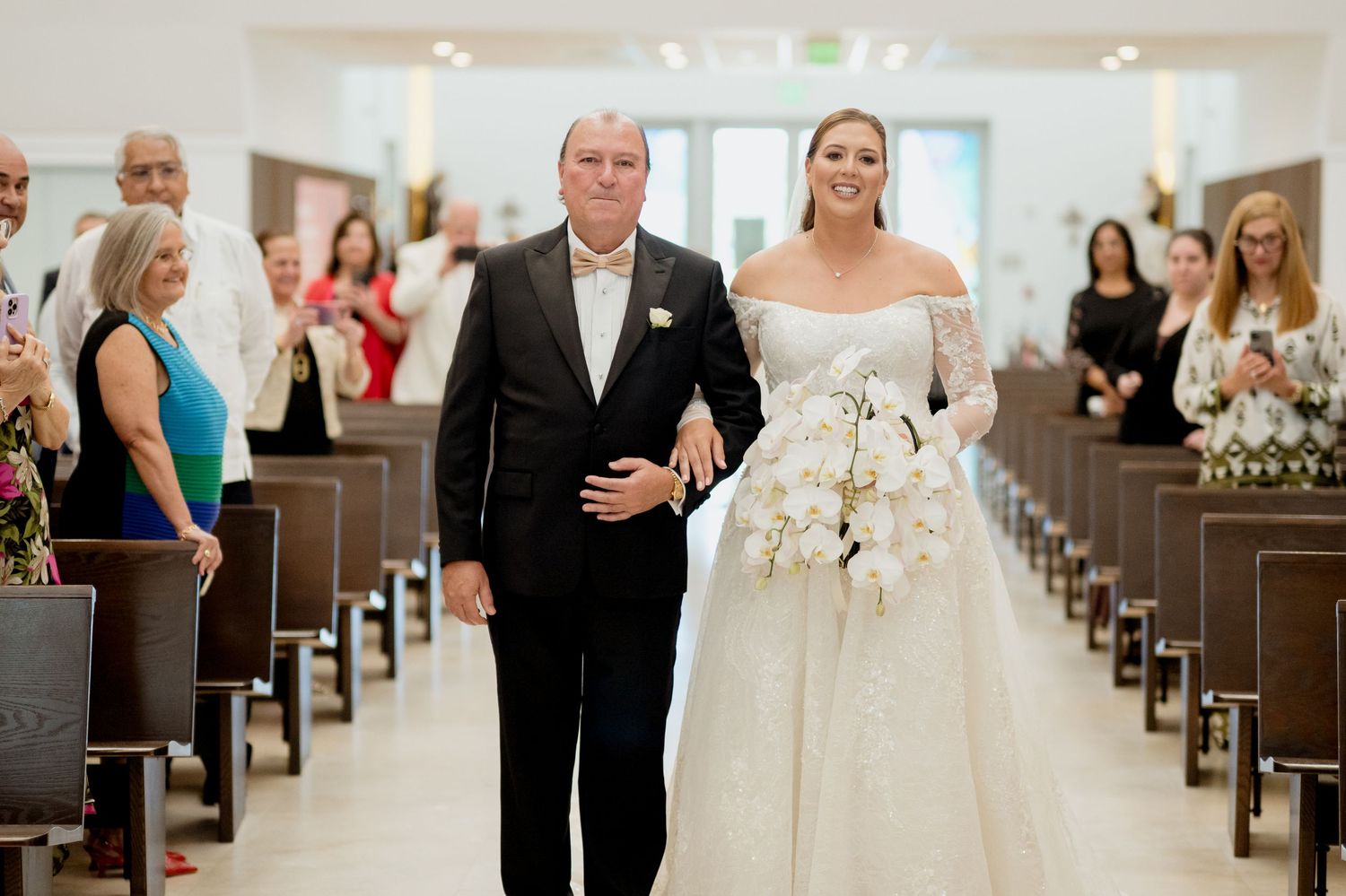 A joyful wedding processional down a church aisle with guests looking on from wooden pews.