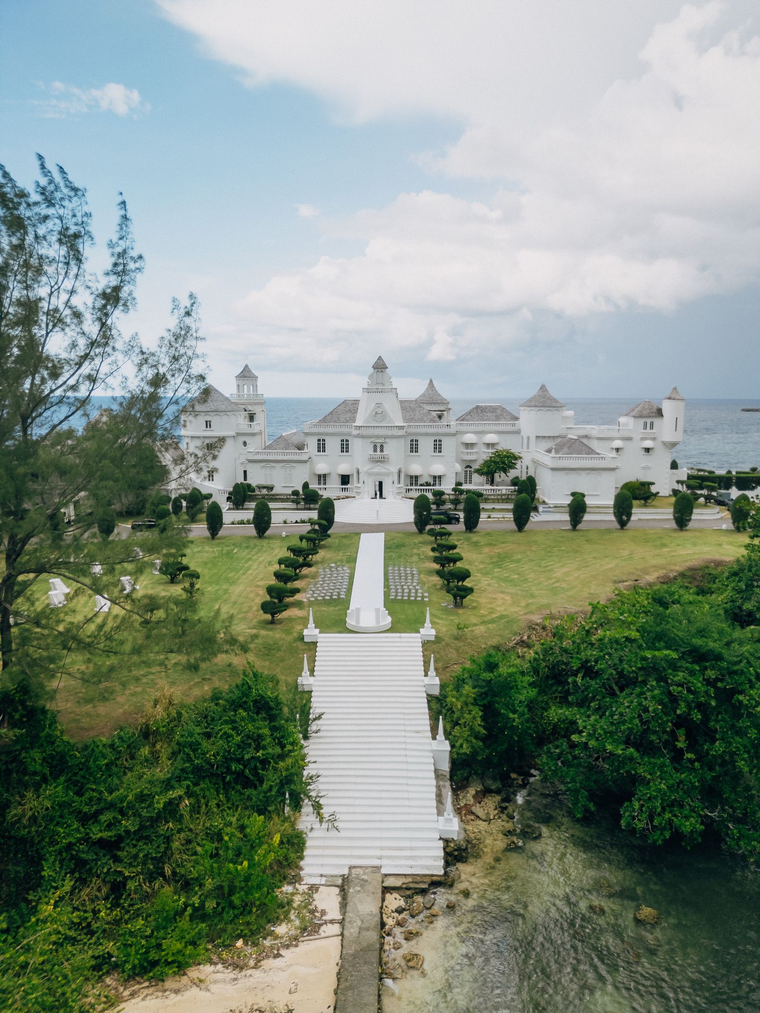 White stone staircase leads to a hilltop temple complex with symmetrical architecture against a blue sky.