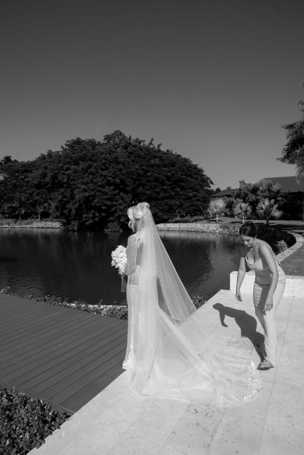 A black and white panoramic sequence of a wedding couple posing by a lake with flowing veil and trees in background.