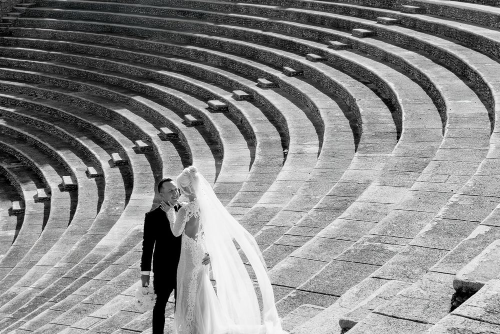 Curved rows of stone seating in an ancient amphitheater form concentric semicircles against a bright sky.