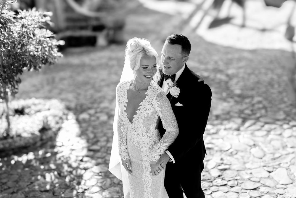 A romantic couple shares a tender moment outdoors during their wedding celebration in black and white photography.