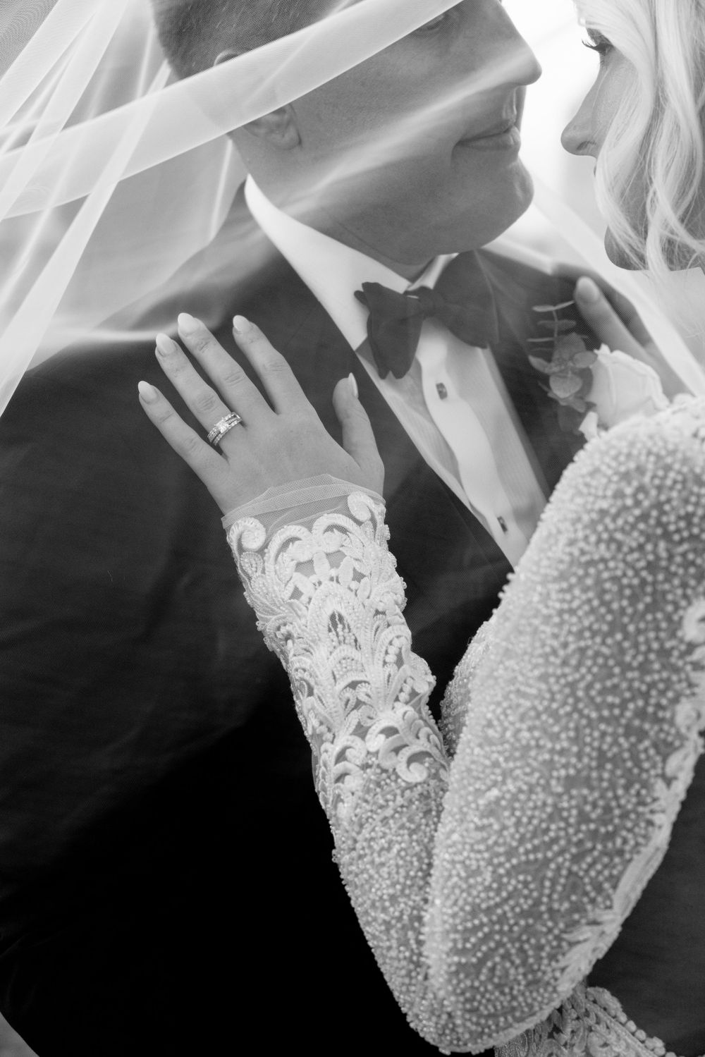 A black and white wedding photo showing an intimate moment with a bride wearing an ornate lace sleeve and veil.