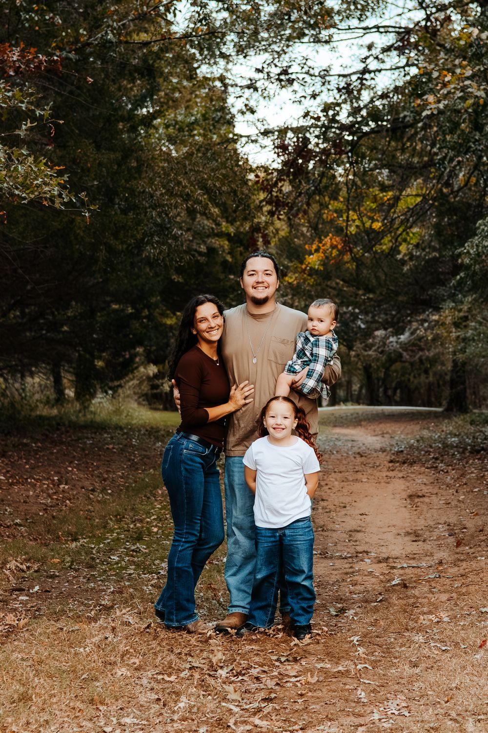 A casual family portrait taken on a dirt path surrounded by autumn trees.