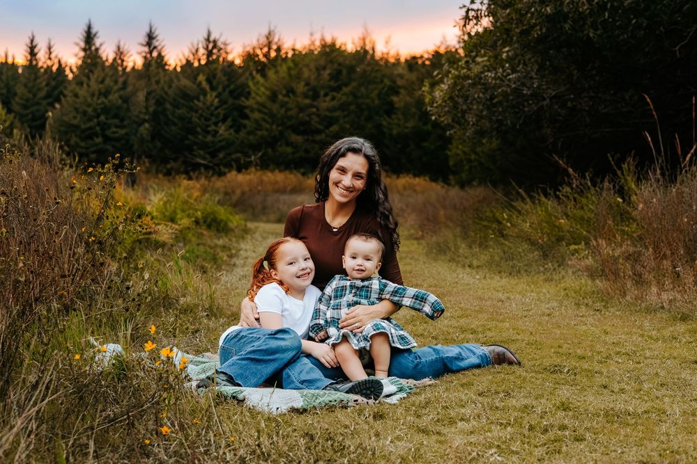 A family lies on a blanket in a grassy field during golden hour sunset.