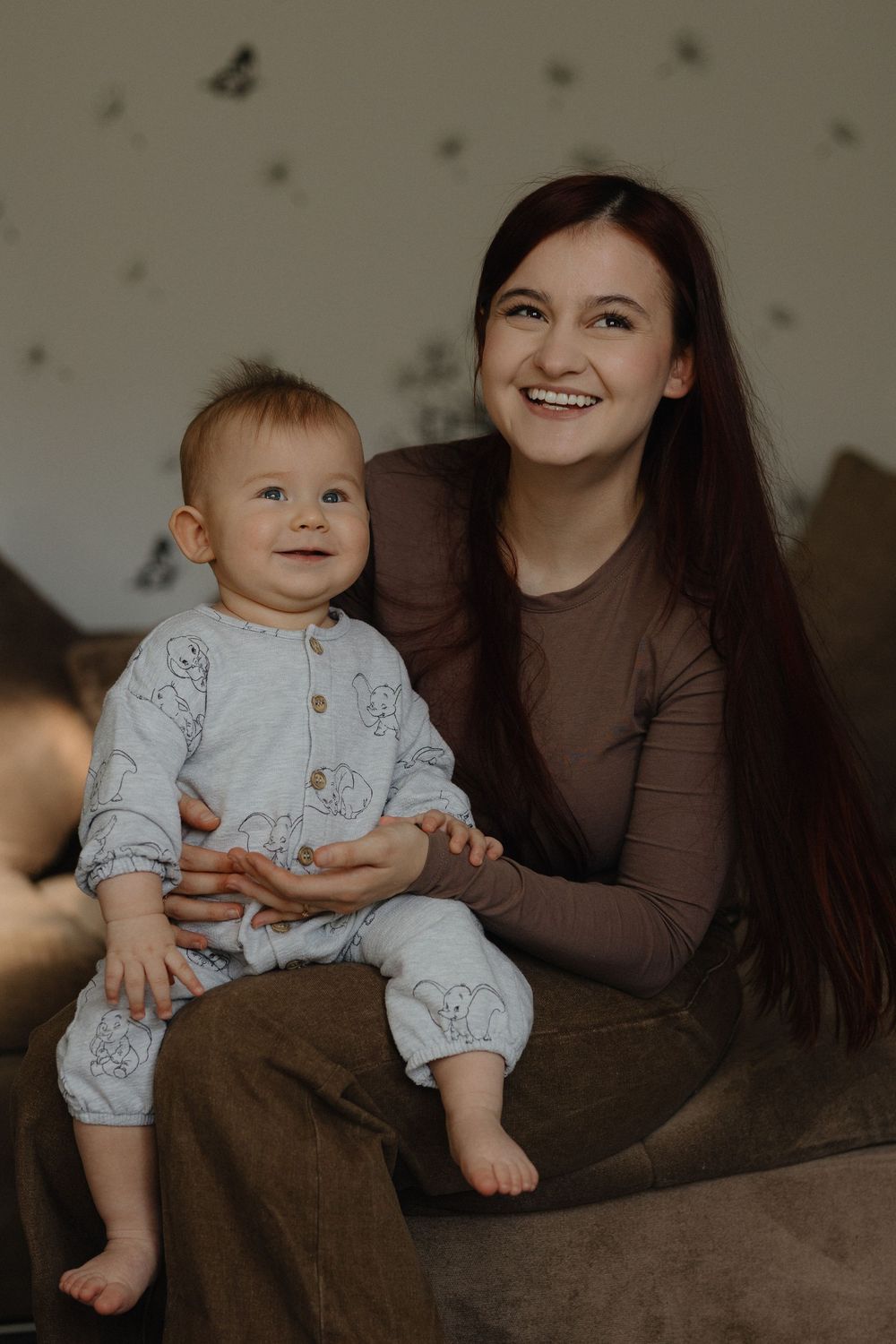 A parent and baby share tender moments together while sitting on a brown couch in warm lighting.
